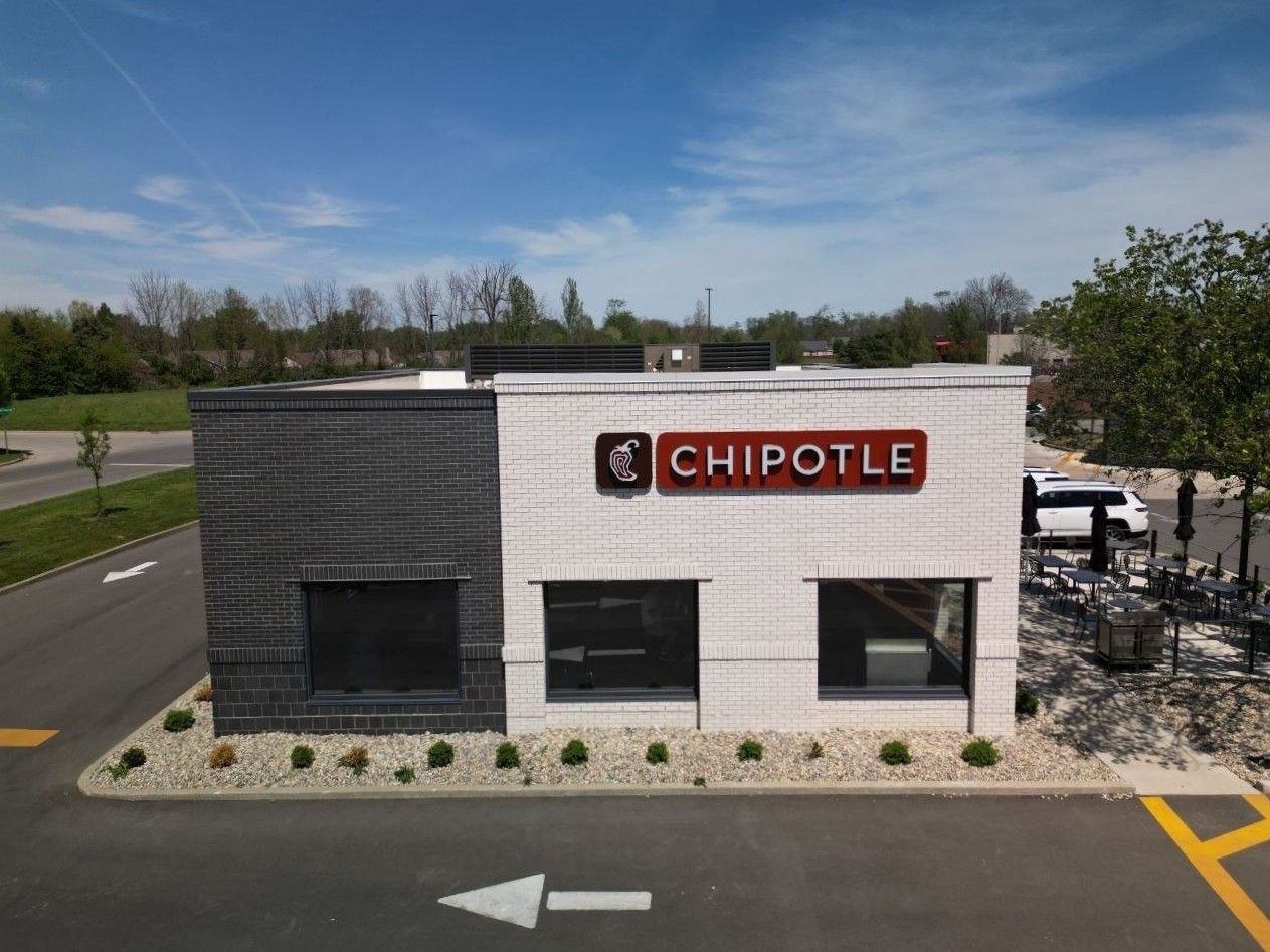 Chipotle storefront with white and gray exterior, red sign, and parking lot in front
