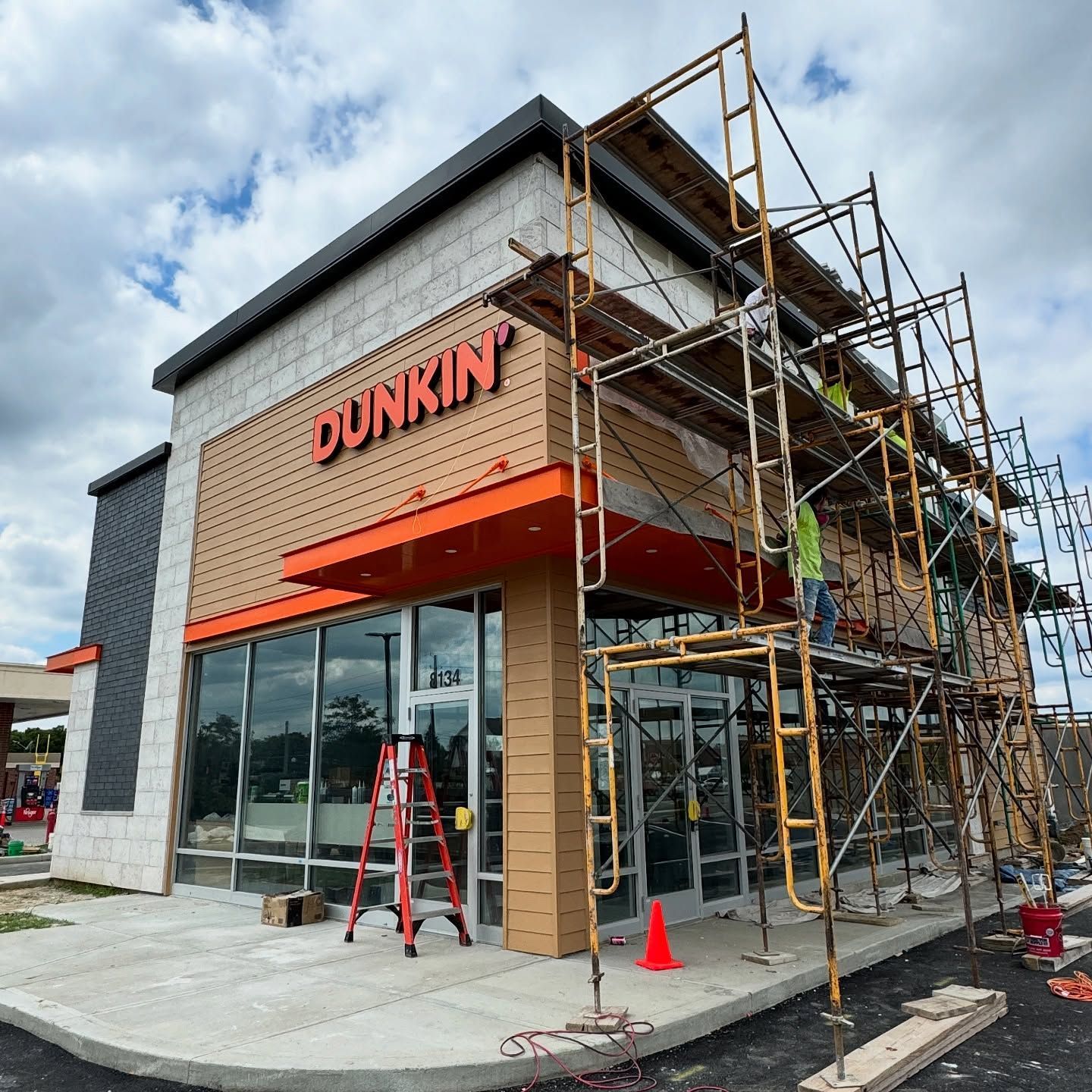A Dunkin’ storefront under construction with scaffolding in front and a ladder nearby.