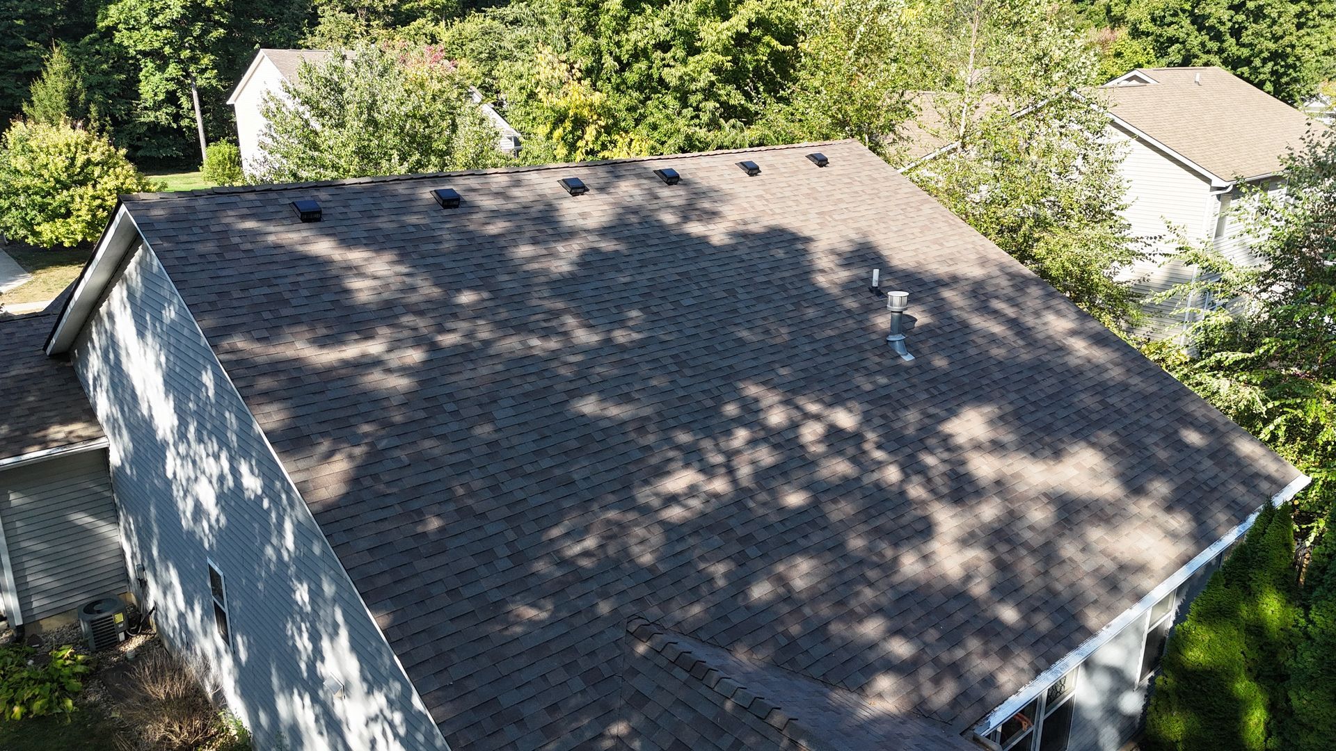 An aerial view of a brown asphalt shingle roof on a house, featuring several ventilation caps along the ridge.