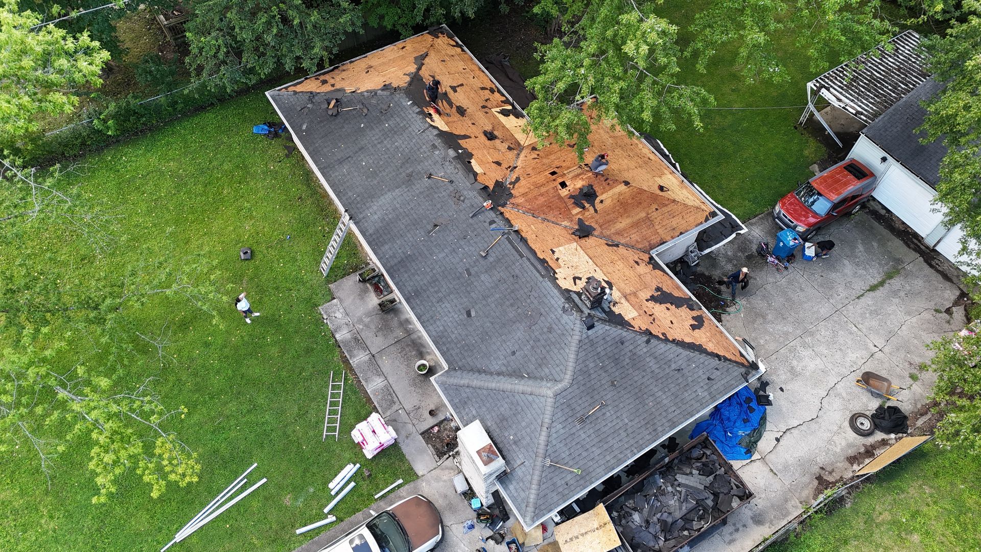 Aerial view of a residential roof under construction with removed shingles, exposed wooden decking, and debris below.