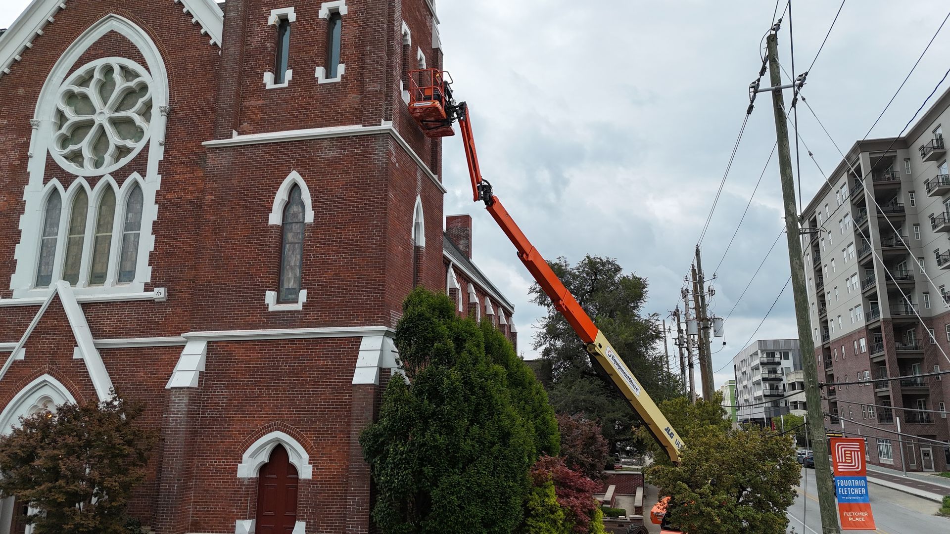 An orange mechanical lift reaches up to the exterior of a red brick church building.